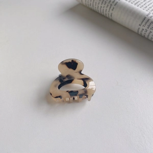Top view of a small tortoiseshell hair claw clip next to a newspaper on white background