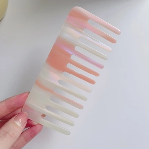 Gros plan d'un peigne à dents larges en acétate marbré rose et blanc tenu à la main
