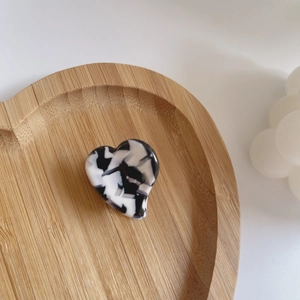 Détail d'une pince à cheveux en acétate en forme de cœur sur un plateau en bois décoratif