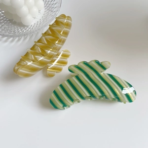 Detail view of large striped hair claws in bright yellow and dark green acetate material