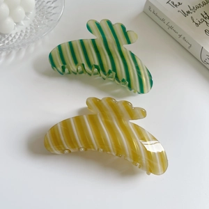 Detail of colorful striped hair claws in green and yellow on a white aesthetic background