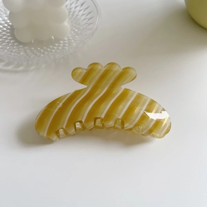 Detail view of yellow hair claw clip with white wavy pattern and glossy resin finish
