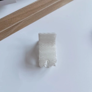 Detail view of mini acetic acid hair claw with white wavy texture and glossy finish