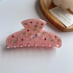 Close-up of pink acetate hair claw clip with colorful rhinestones and floral pattern details