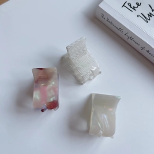 Three acetate mini hair claws in marble and chevron patterns on a white table