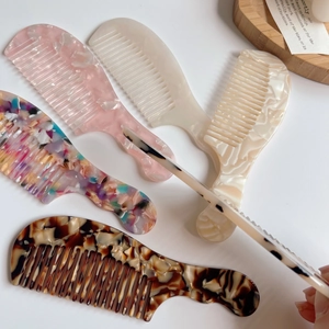 Peignes à cheveux élégants en acétate marbré rose et écaille sur un plateau en bois