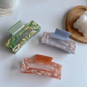 Three large acetate hair claws in green, blue, and pink with marble textures and hollow design
