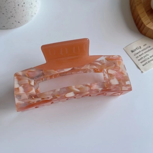 Detail of large square cutout hair claw clip in pink and orange marble acetate finish