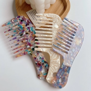 Three acetate wide-tooth hair combs in artistic floral, marble, and purple cloud patterns