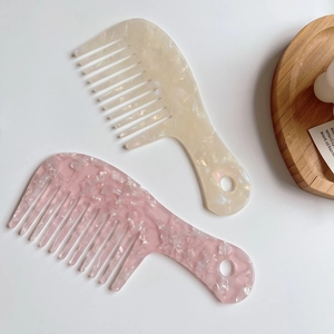 Detailed view of two acetate wide-tooth combs in marble cream and pink on a tray