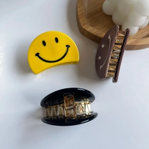 Trois pinces à cheveux à motif smiley en jaune, café et noir sur un plateau en bois