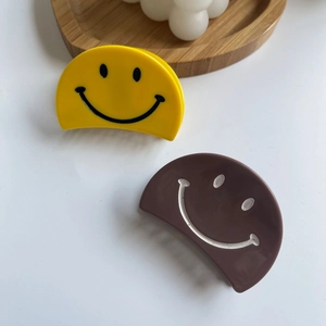 Gros plan de pinces à cheveux mates jaune et café avec motif sourire minimaliste