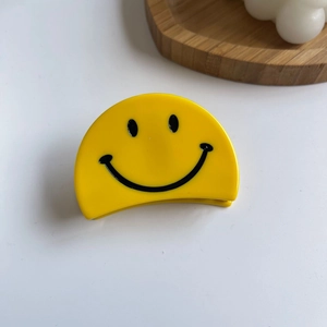 Gros plan d'une pince à cheveux jaune en demi-cercle avec un motif de smiley mignon