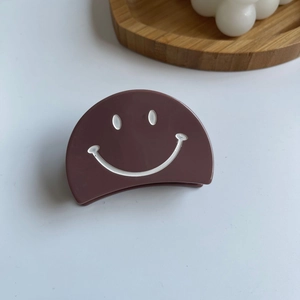 Vue détaillée d'une pince à cheveux marron chocolat ornée d'un motif visage souriant blanc