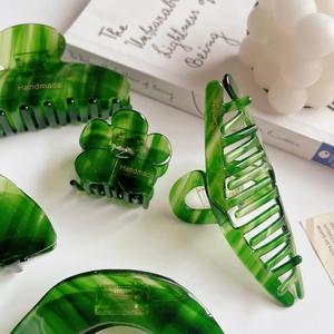 Macro shot of green marble acetate hair claws with premium handmade gold lettering detail