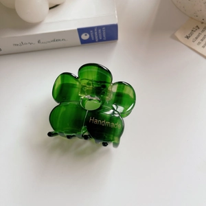 Macro detail of a green acetate flower hair claw with gold handmade lettering and metal spring
