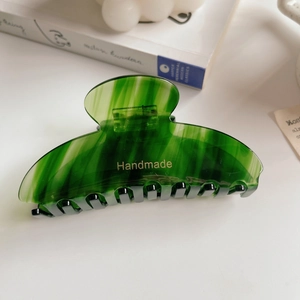 Close-up of green marble acetate hair claw clip with golden handmade logo on a book
