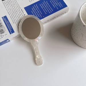Handheld vanity mirror with shell luster finish and wavy edges on a white desk