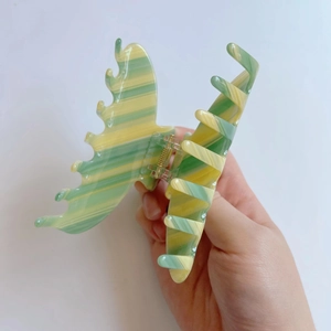 Detail of butterfly claw clip with green and yellow striped acetate pattern and gold spring