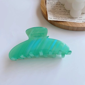 Detailed macro view of a green acetate hair claw clip with blue diagonal stripes