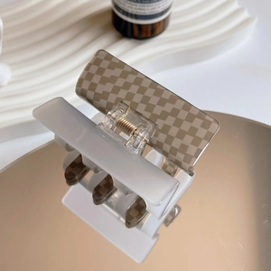 Close-up of checkered acetate hair claw clip with golden metal spring on a reflective surface