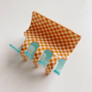 Detailed view of checkered acetate hair claw clip with orange and white pattern and glitter