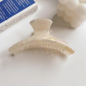 Macro shot of curved acetate hair claw clip with pearlescent finish and golden logo