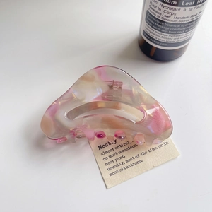 Detail view of pink marble acetate hair claw clip with golden metal spring on desk