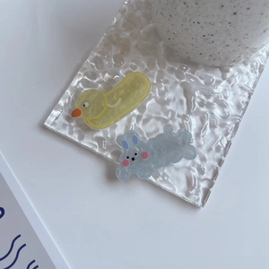 Cute resin hair clips with yellow duck and blue rabbit shapes on a clear glass tray