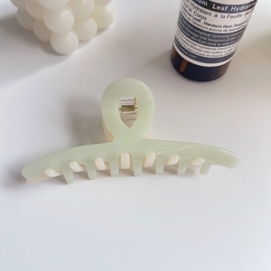 Détail de la pince à cheveux vert menthe avec ressort doré sur une surface blanche