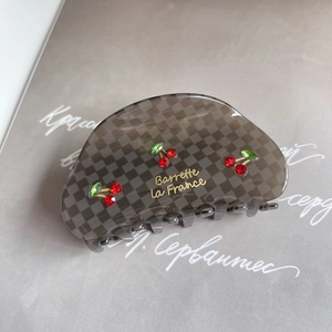 Close-up of gray checkered hair claw clip with cherry rhinestone design and gold label