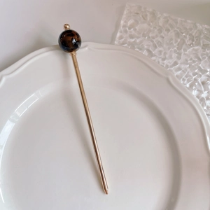 Close-up of golden hair stick with a tortoiseshell patterned bead on white ceramic tray