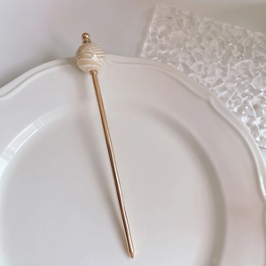 Detail of a minimalist gold hair stick with a marble-textured acetate round sphere