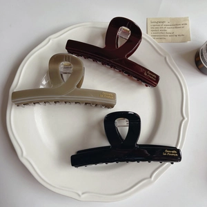 Three large tortoiseshell hair claws in burgundy, olive, and black on a ceramic tray