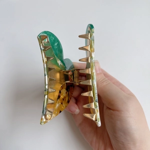 Detail of green and amber marbled acetate hair claw clip with golden metal teeth