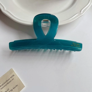 Detailed close-up of dark teal translucent acetate hair claw with gold lettering text