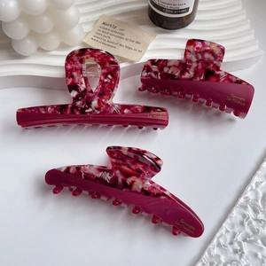 Detail view of large acetate hair claws with pink marble pattern and gold lettering