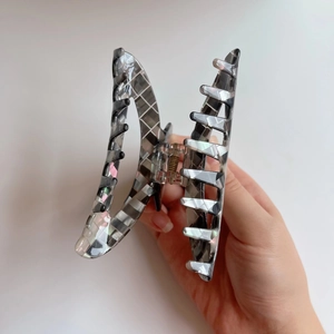 Dettaglio della grande molletta per capelli in acetato con motivo a mosaico grigio e molla