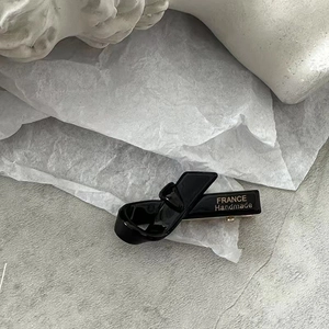 Détail d'une barrette nœud noire brillante faite à la main avec étiquette dorée