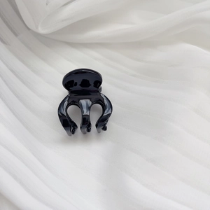 Macro shot of a small black acetate hair claw clip with a high-gloss finish on white fabric