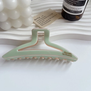 Detail of mint green and pink acetate hair claw clip with gold lettering on white stand