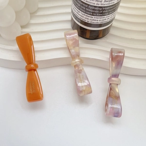 Three-piece set of acetate bow hair clips in orange and marble textures on display
