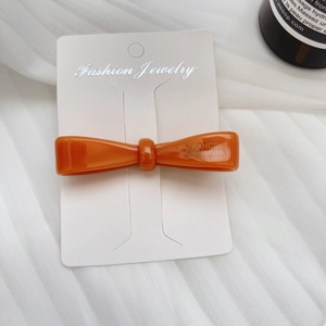 Detail of orange acetate bow hair clip with gold France Handmade text on display card