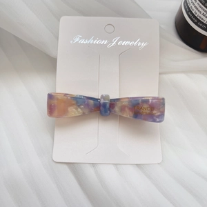 Detail of a handmade acetate bow hair clip with purple and orange textures on display card