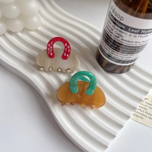 Detail of purse-shaped acetate hair claws on a tray with lifestyle props and soft lighting