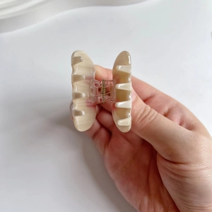 Detail shot of a cream marble acetate hair claw with a gold metal spring held in hand