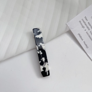 Detail of a rectangular acetate hair clip with black and white marble pattern on white fabric