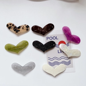 Dettaglio di fermagli per capelli a cuore in acetato con lettere incise multicolore