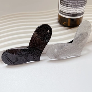 Dettaglio di fermagli per capelli a cuore glitterati in nero e argento su supporto a onde