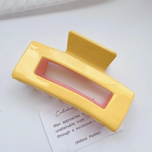 Detail view of yellow and pink contrast acetate hair claw clip on minimalist background